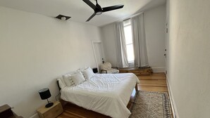 A bedroom with a bed, a nightstand, a lamp, a ceiling fan, a window with curtains, and a wooden floor. - Lawless Rico: Engel Room (Rico)