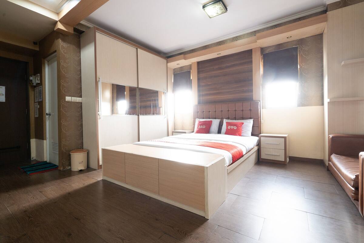 Un dormitorio con una cama grande, una mesita de noche, suelo de madera y una ventana con cortinas.