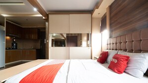 Une chambre d’hôtel moderne avec un grand lit, une tête de lit en bois et une vue sur la cuisine.