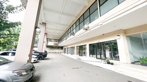 Un espace de stationnement avec plusieurs voitures, un bâtiment doté de grandes fenêtres et des plantes en pot disposées le long du trottoir.