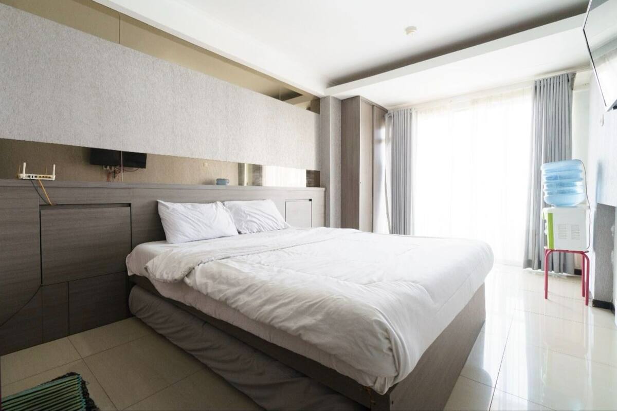 Una habitación de hotel moderna con una cama grande, un televisor de pantalla plana en la pared y vistas al exterior por la ventana.