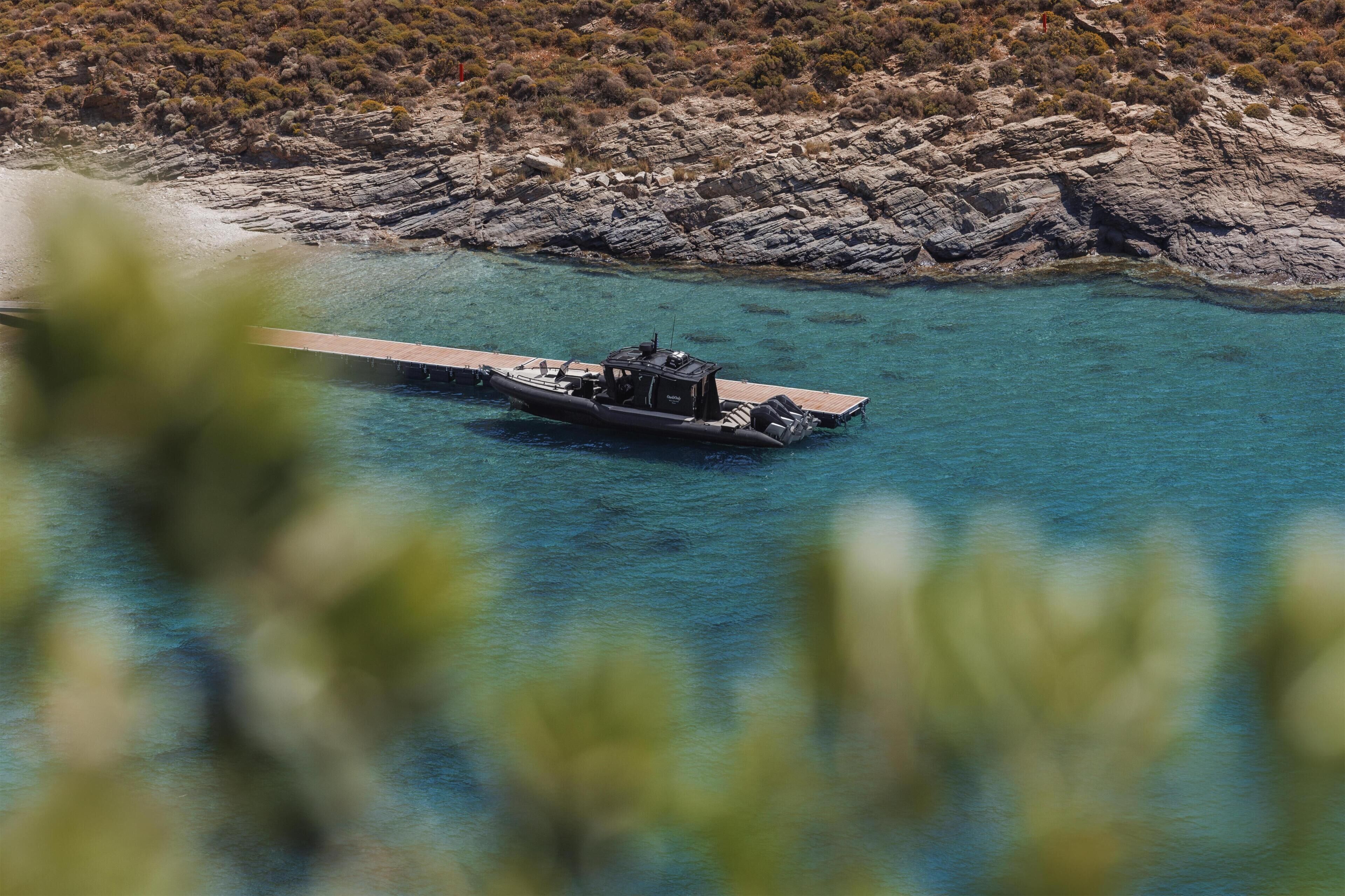 A boat docked at a pier with rocky terrain and sparse vegetation in the background.