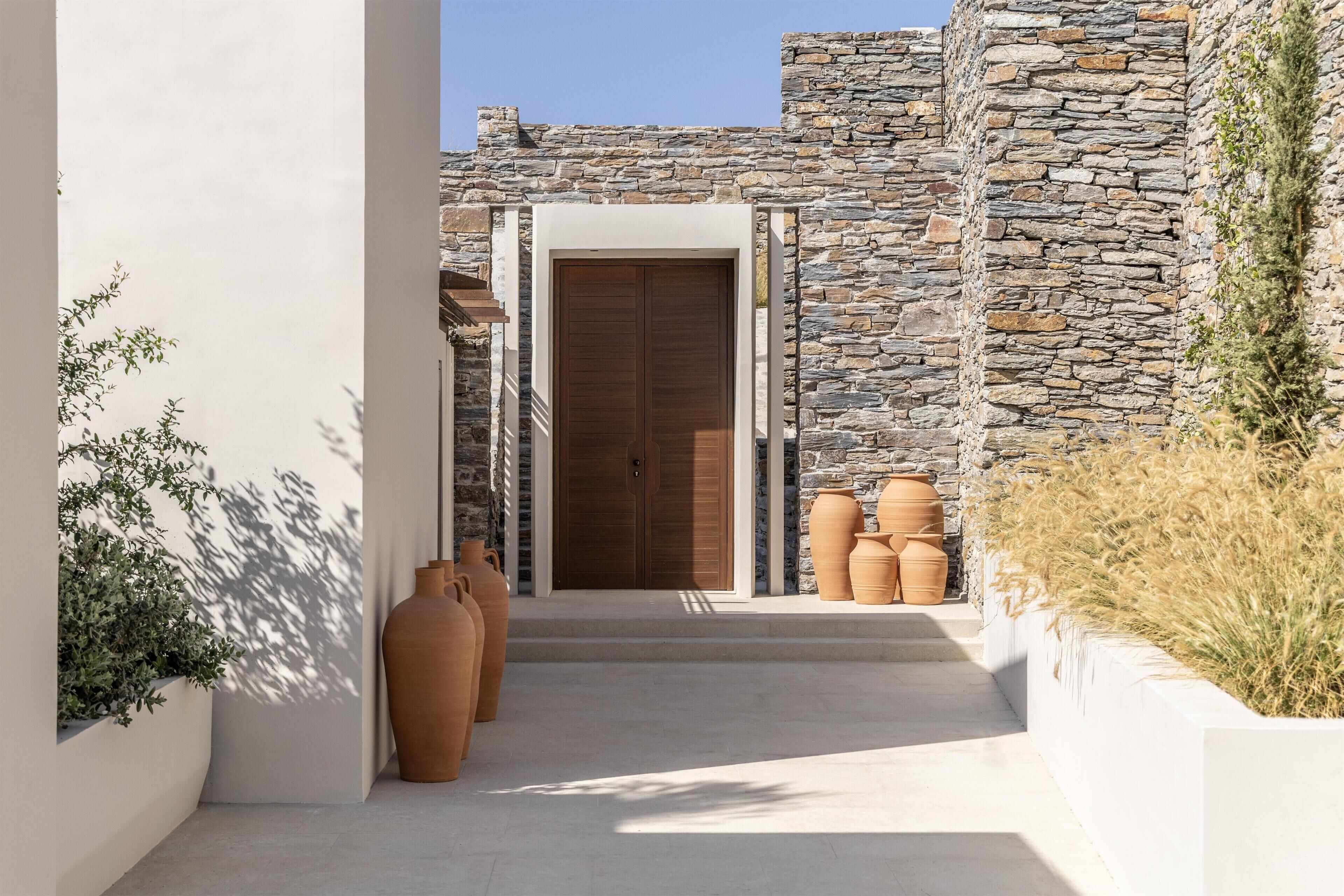 A stone building with a wooden door, terracotta pots, and a narrow pathway.