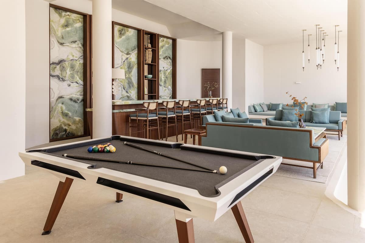 A pool table with a green felt surface, a seating area with blue sofas, and a bar with wooden chairs.