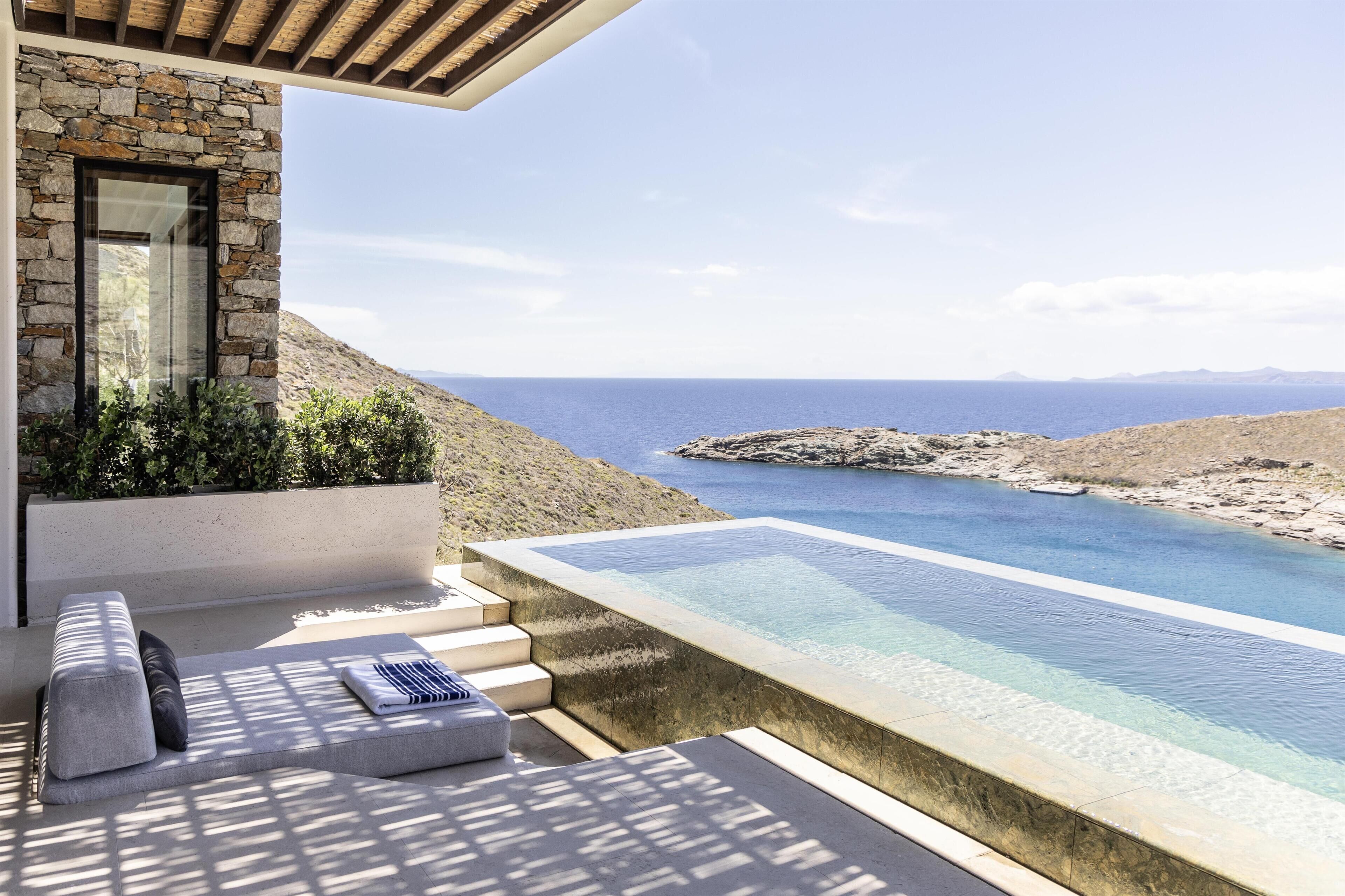 A modern outdoor pool area with a stone wall, seating, and a view of the sea.