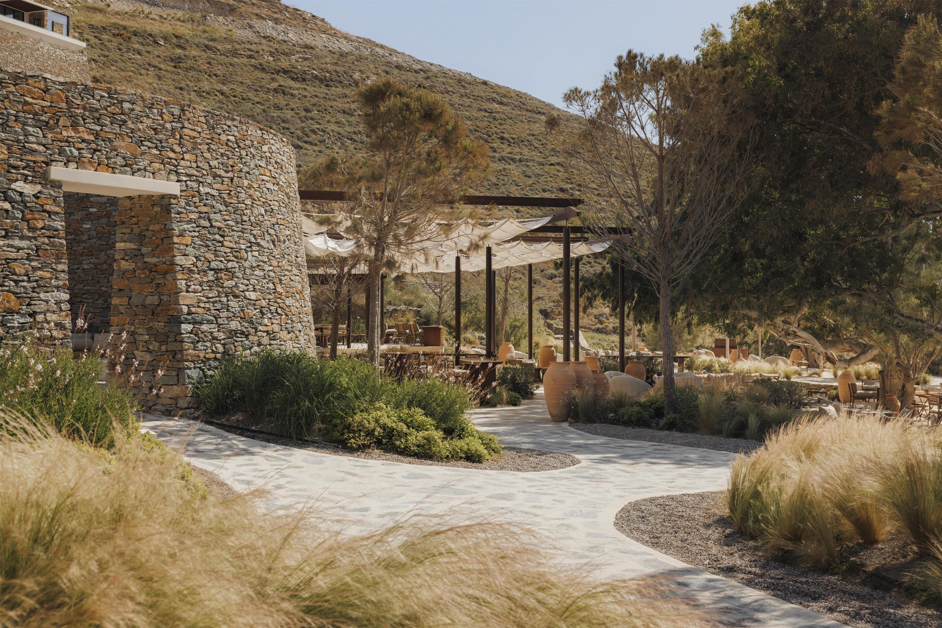 A stone building with a patio area, outdoor seating, and a mountainous backdrop.