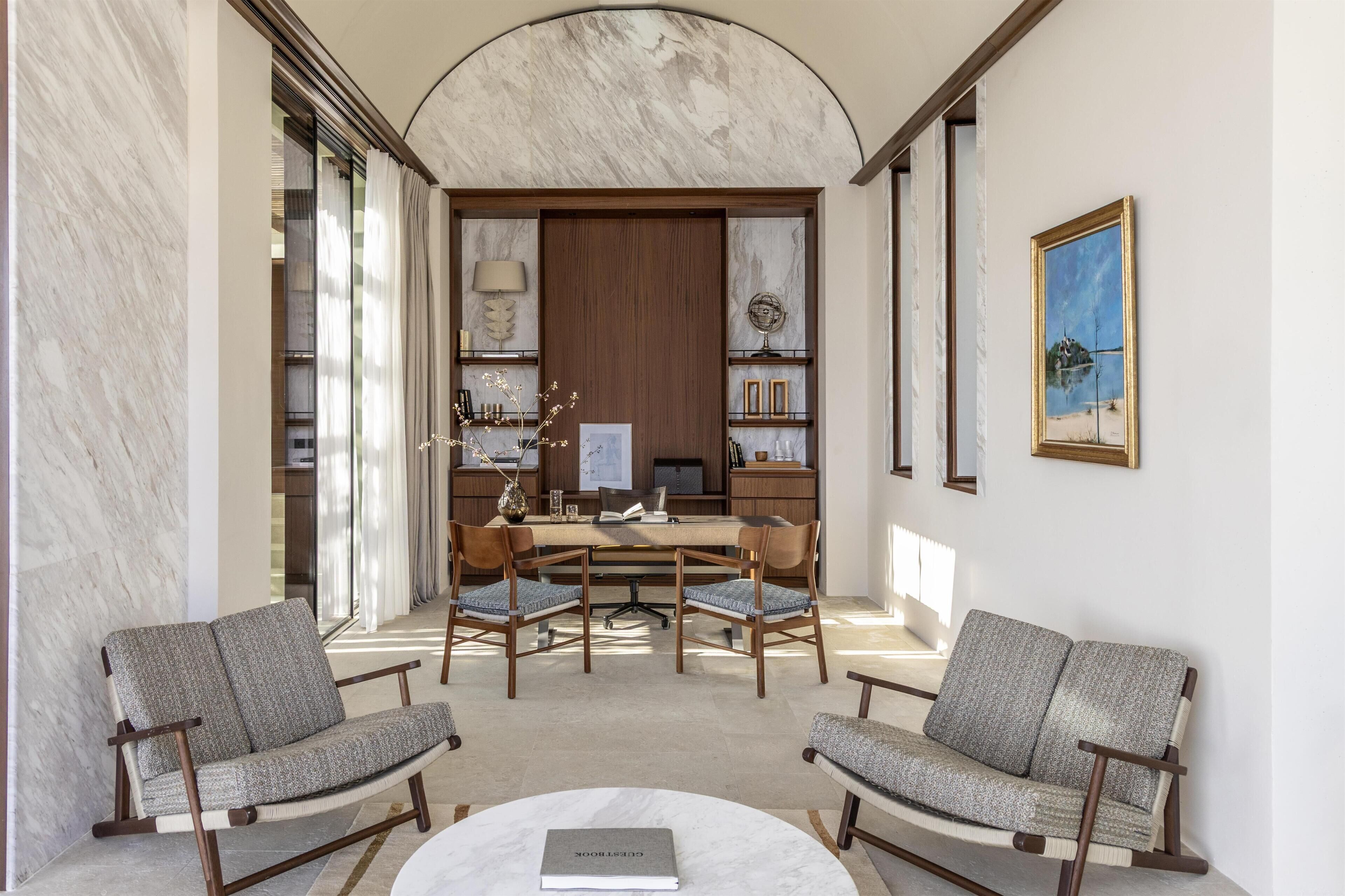 A modern interior with a marble wall, a wooden desk, two upholstered chairs, and a round coffee table.