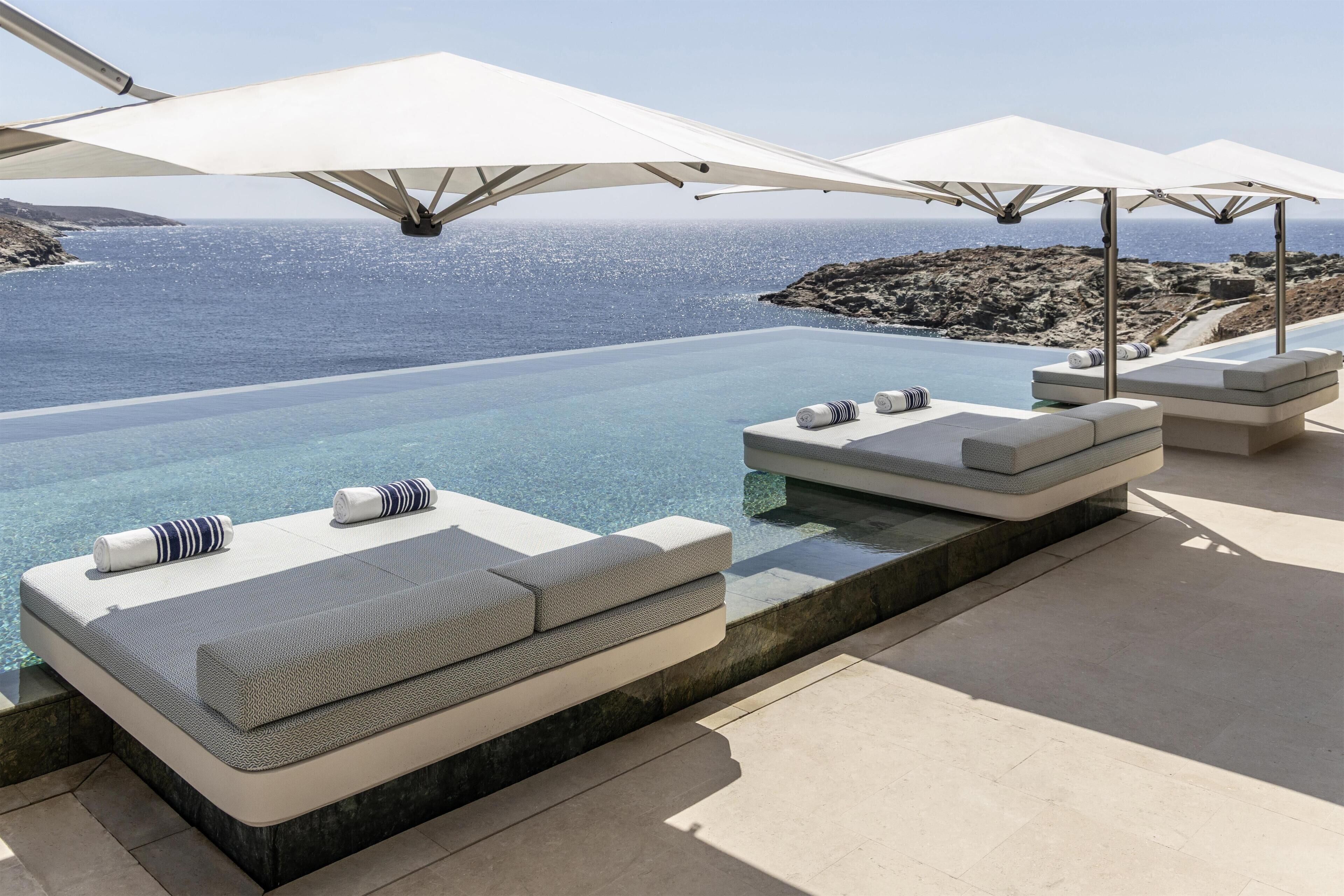 Zona de piscina con vistas al mar, mobiliario exterior y sombrillas.