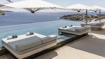 Zona de piscina con vistas al mar, mobiliario exterior y sombrillas.