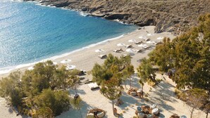 Vue aérienne d’une plage avec des transats, des parasols et une côte rocheuse.