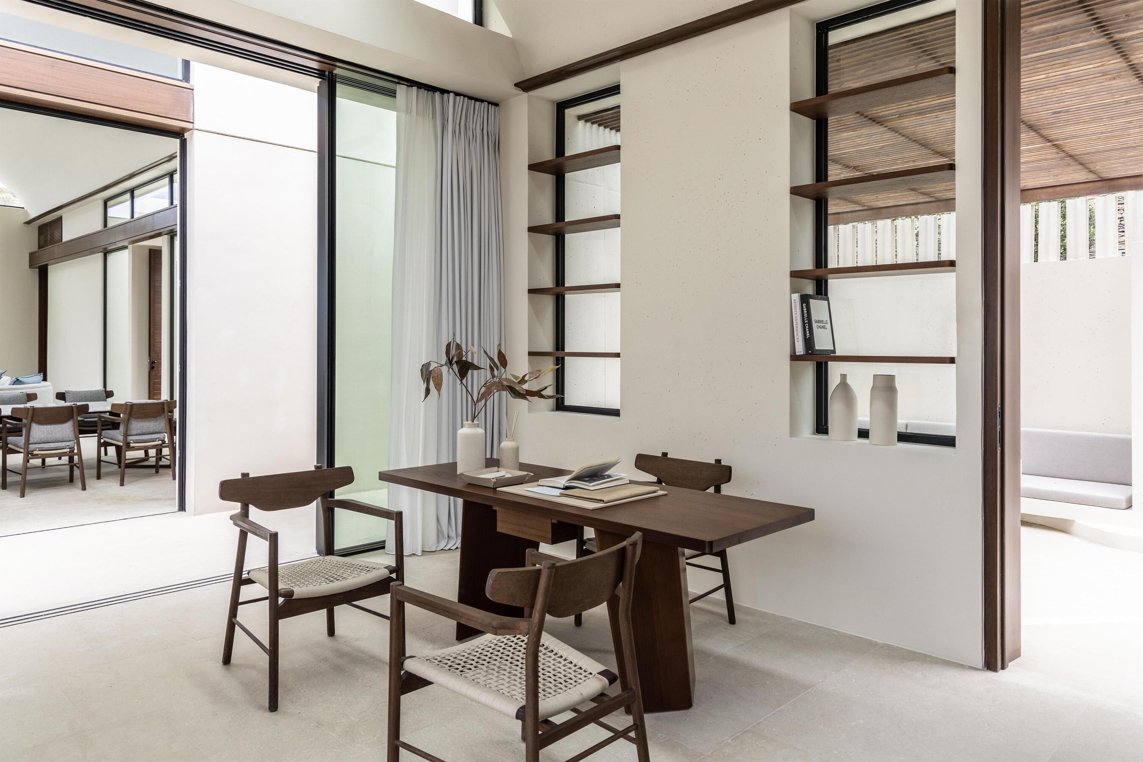 A modern dining area with a wooden table and chairs, a bookshelf, and a large window with curtains.