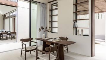 A modern dining area with a wooden table and chairs, a bookshelf, and a large window with curtains.