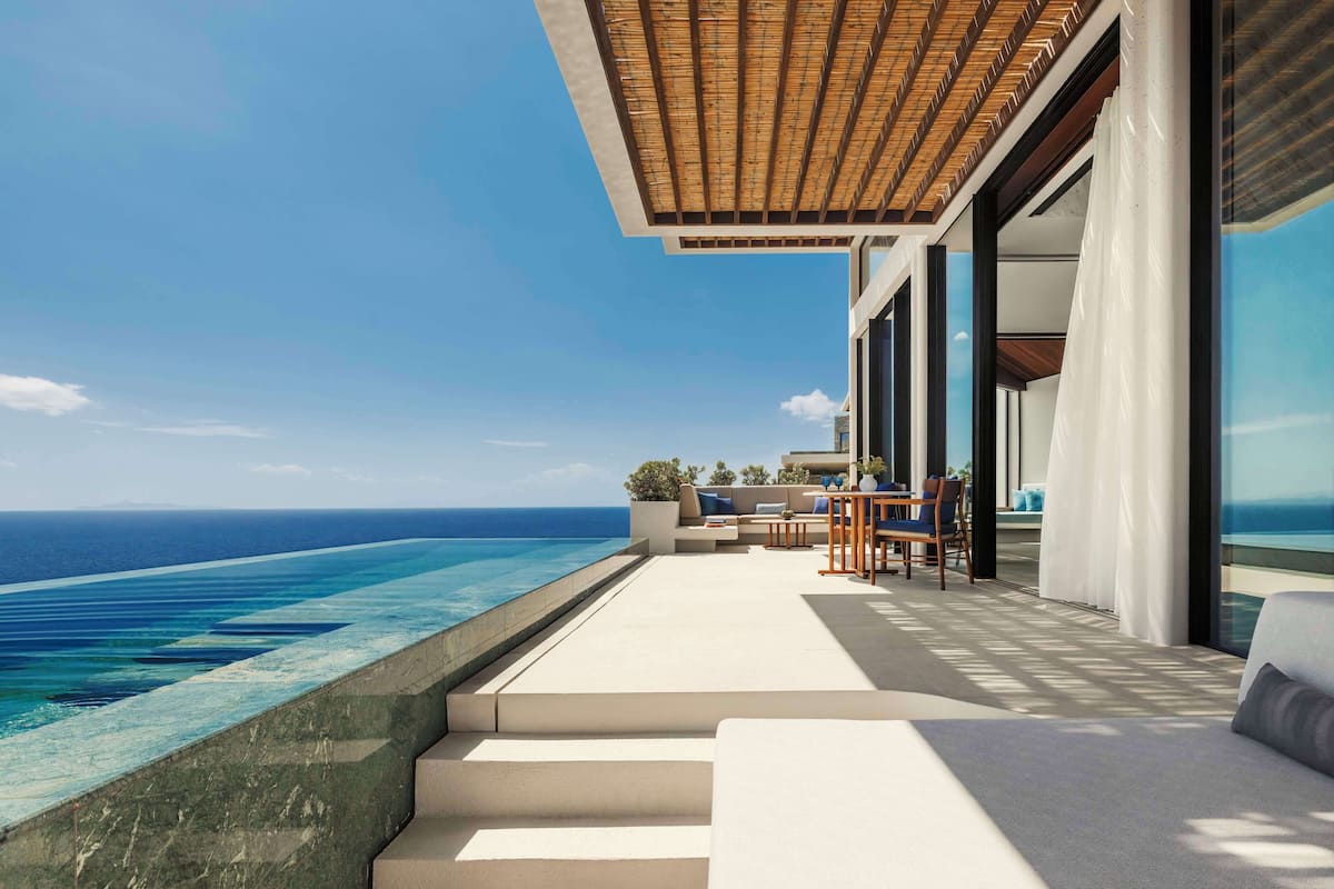 A modern outdoor lounge area with a view of the ocean, steps leading to a seating area, and a covered section with a wooden ceiling.