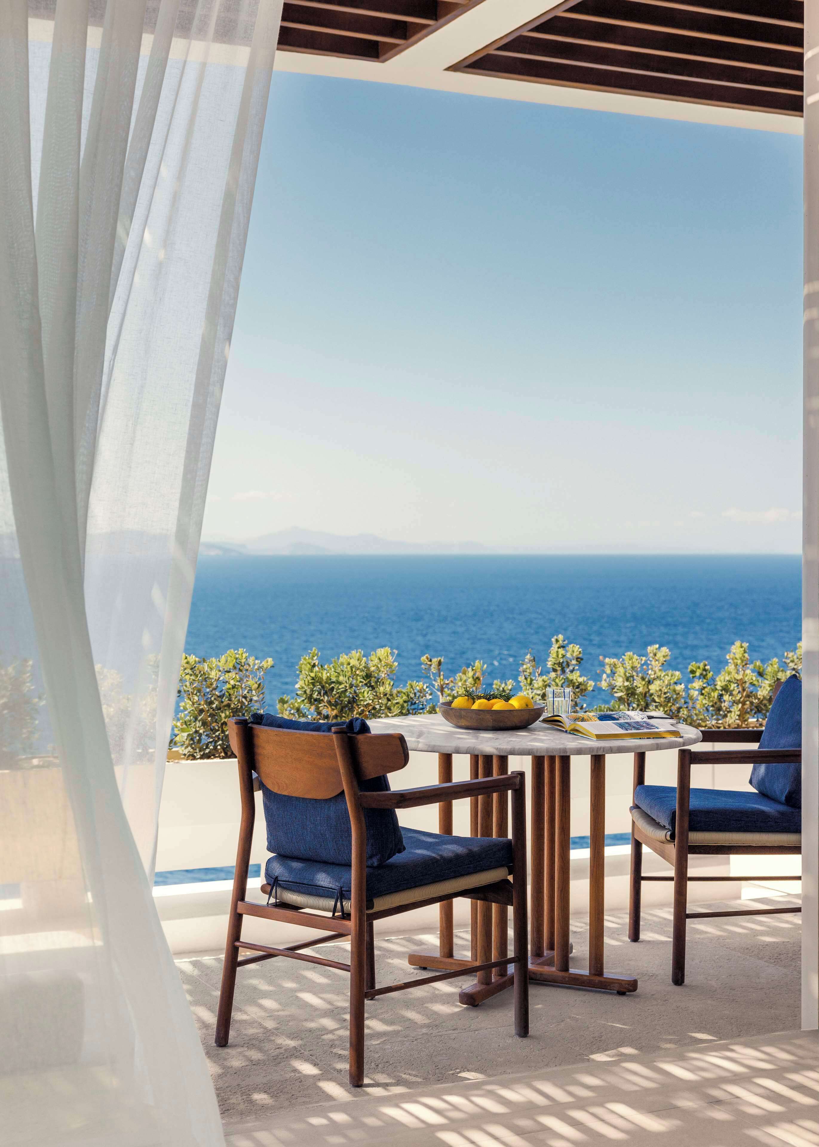 Une terrasse avec une table et des chaises, un saladier rempli de fruits et une vue sur la mer.