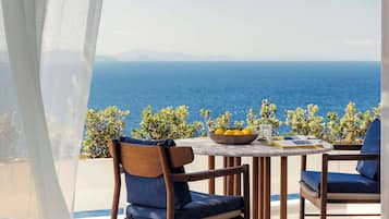 Una terraza con mesa y sillas, un frutero y vista al mar.