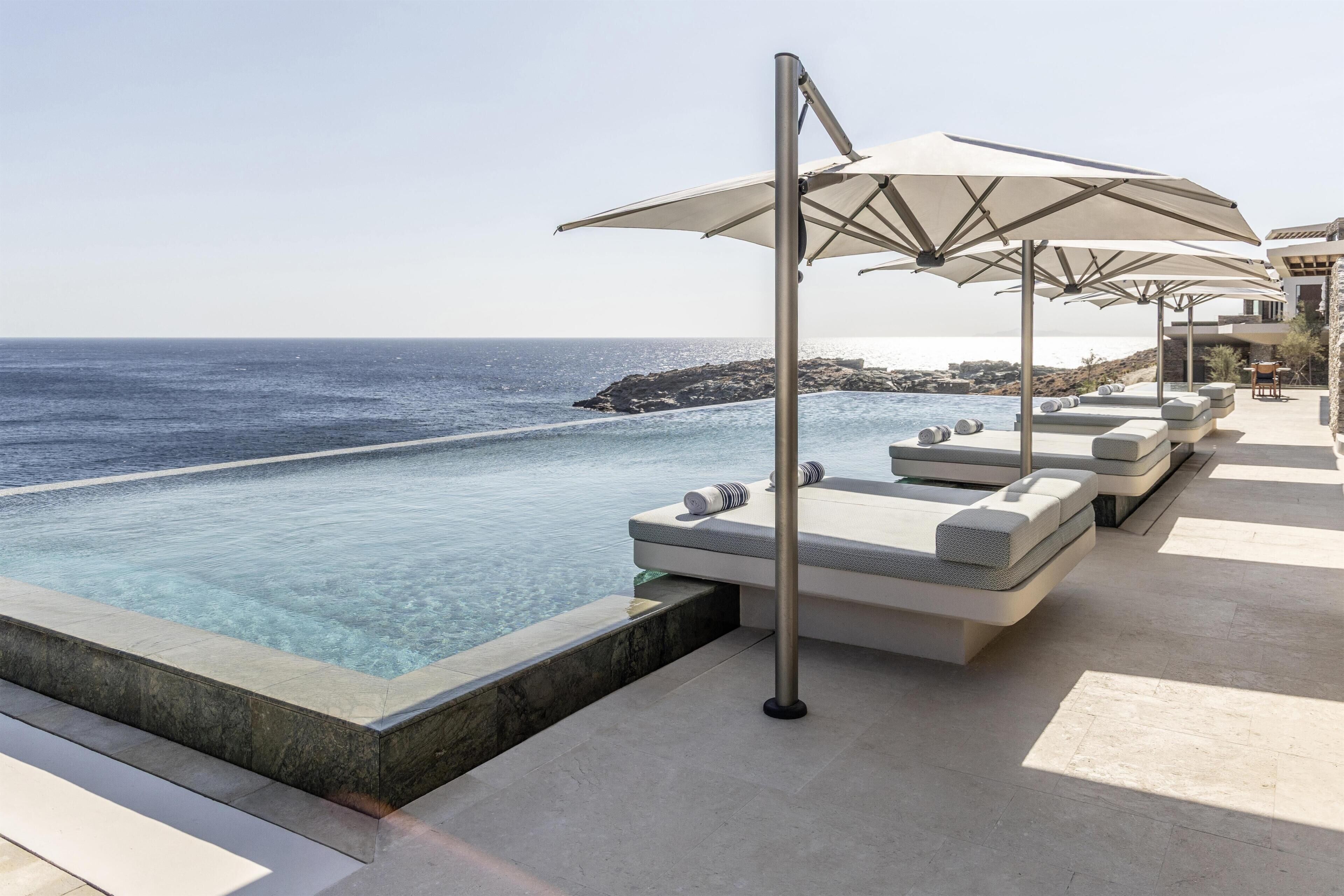 A poolside area with lounge chairs and umbrellas, overlooking a clear blue sea.