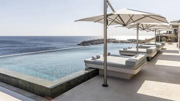 A poolside area with lounge chairs and umbrellas, overlooking a clear blue sea.