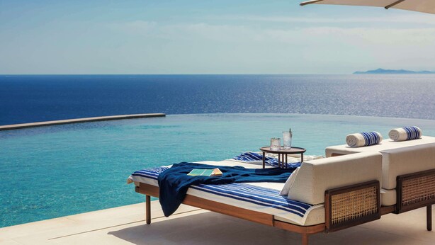 Un salon de bord de piscine avec vue sur la mer, une chaise longue, une petite table et un parasol.
