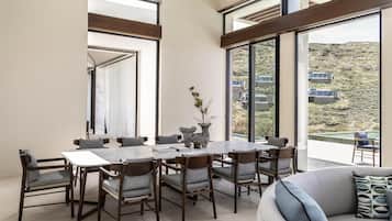 Un comedor moderno con una mesa grande y sillas, ventanas amplias y vistas a un paisaje montañoso.