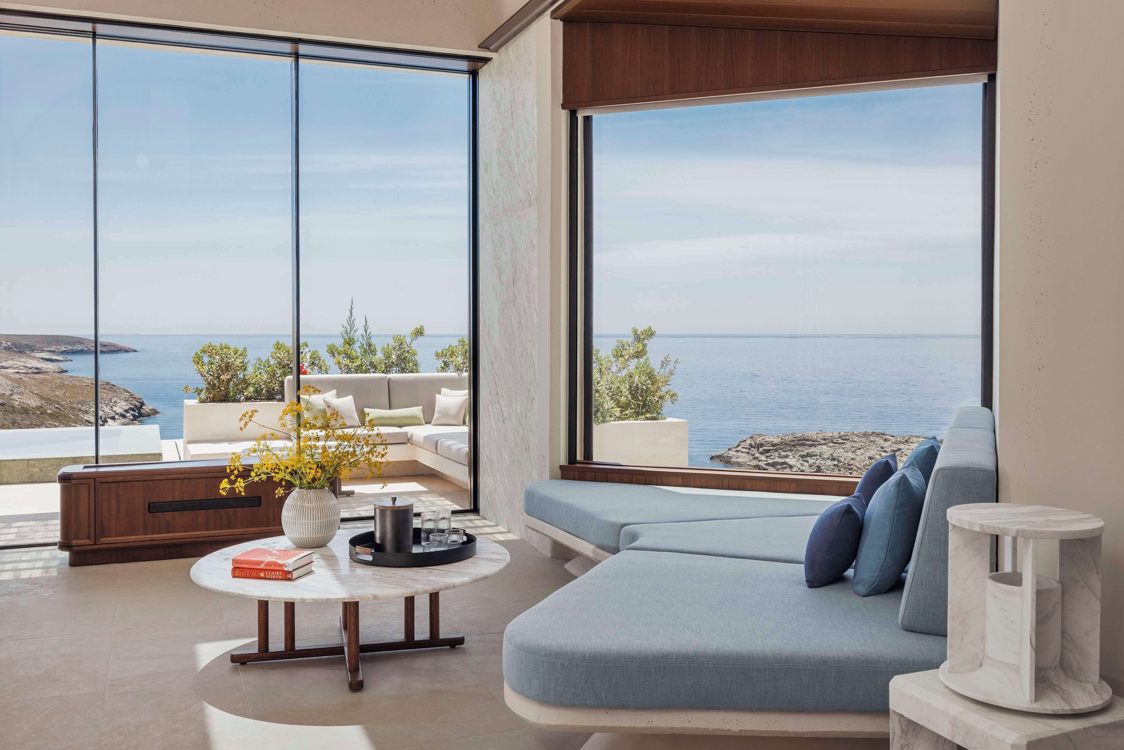 A modern living room with a large window overlooking the sea, a sofa, a coffee table, and a vase with flowers.