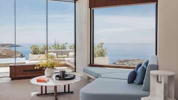A modern living room with a large window overlooking the sea, a sofa, a coffee table, and a vase with flowers.