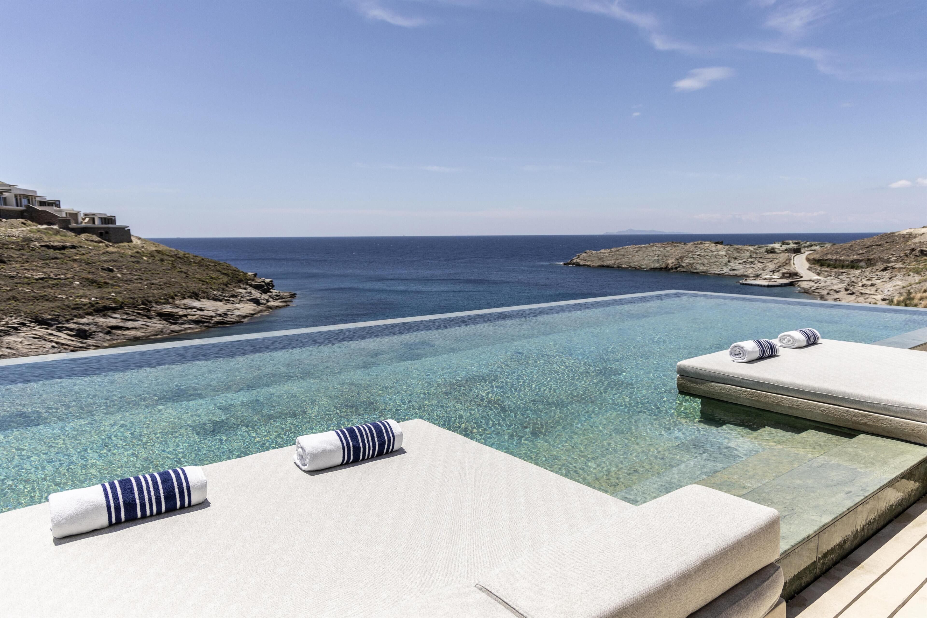 Une piscine à débordement à l’eau cristalline, dotée de chaises longues et de serviettes.