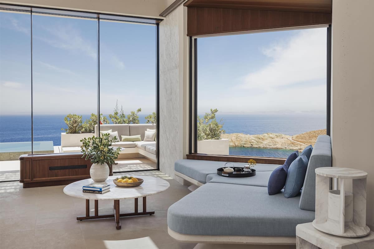 A modern living room with a large window overlooking the sea, a sofa, a coffee table, and a small side table.