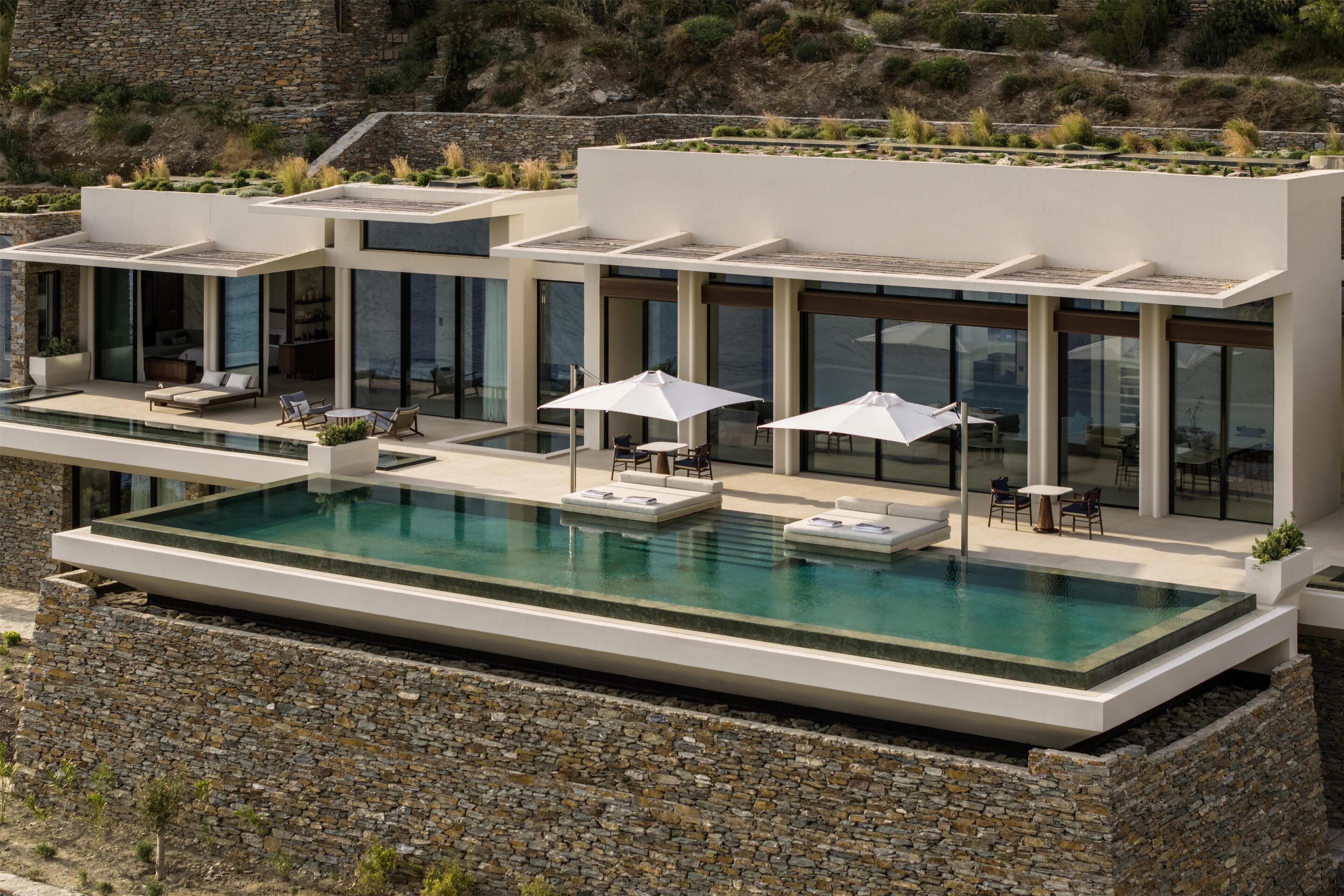 Un bâtiment moderne doté d’une piscine à débordement sur le toit, d’un espace extérieur aménag é et d’un mur de soutènement en pierre.