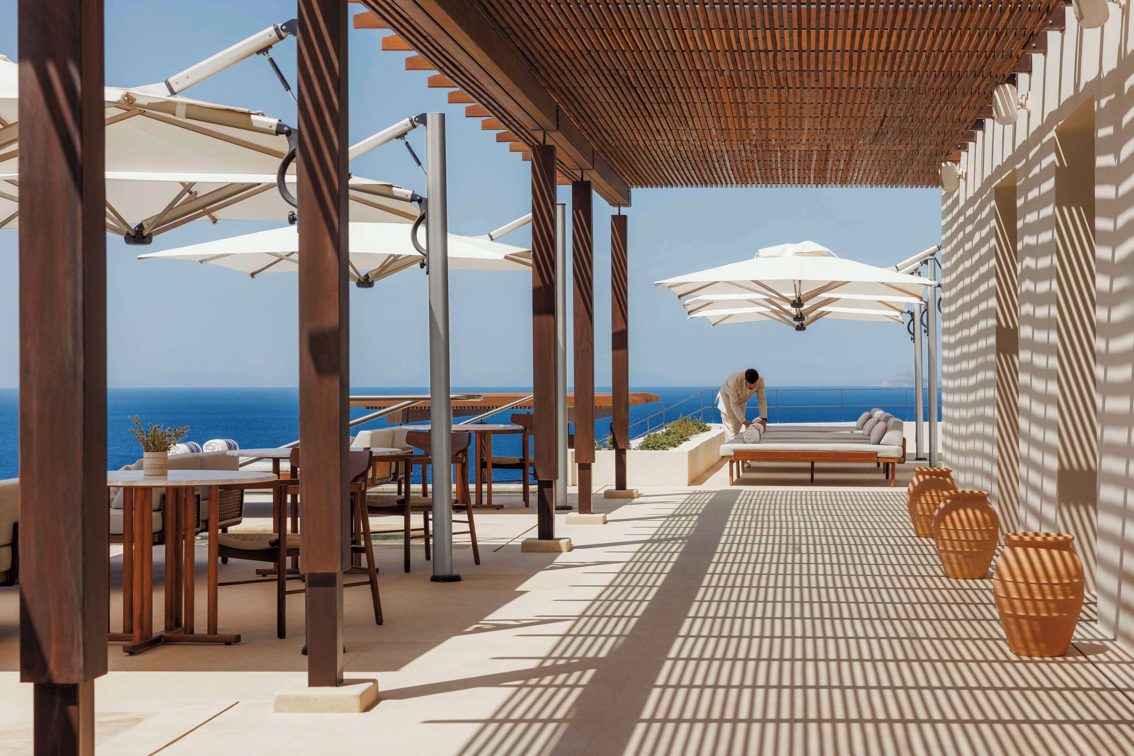 A covered outdoor seating area with tables and chairs, umbrellas, and a view of the ocean.