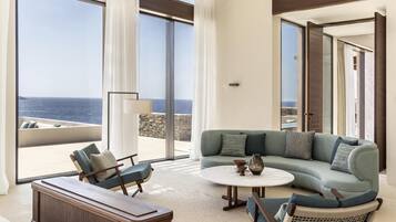 Una sala de estar moderna con un amplio ventanal con vista al mar, un sofá, una mesa de centro y una mesita de madera.