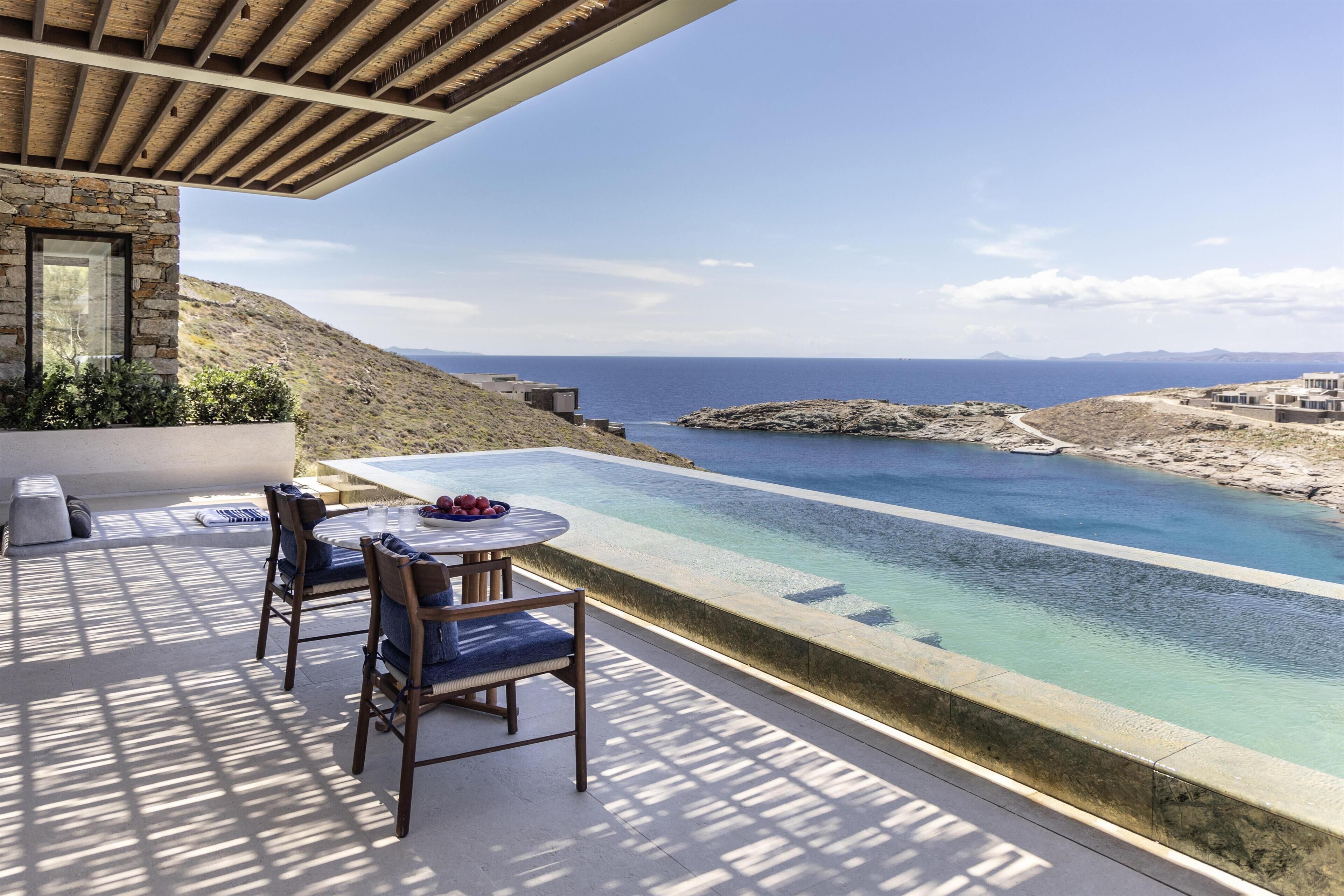 A terrace with a pool, chairs, and a table overlooking a coastal landscape.