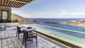 A terrace with a pool, chairs, and a table overlooking a coastal landscape.