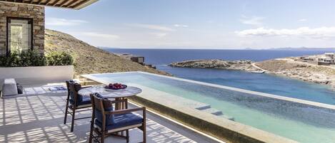 A terrace with a pool, chairs, and a table overlooking a coastal landscape.