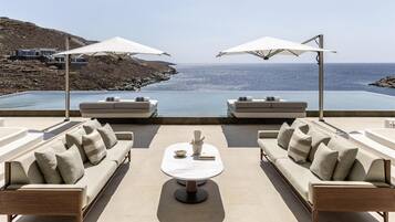 A modern outdoor seating area with a view of the sea, featuring sofas, a table, and umbrellas.