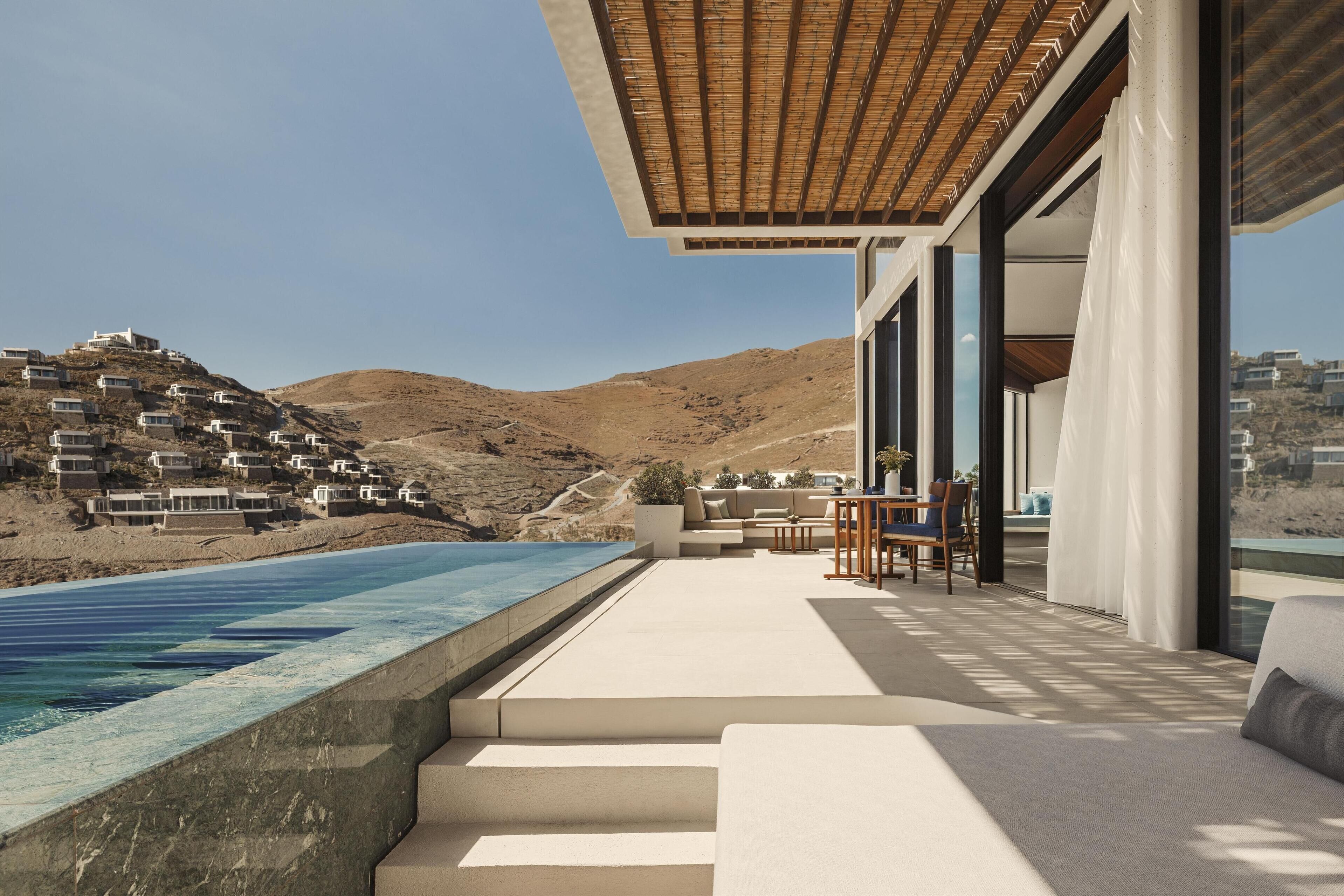 A modern outdoor living area with a pool, steps leading to a seating area, and a view of a hillside with buildings.