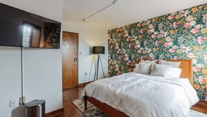 Een slaapkamer met een houten bed, een aan de muur bevestigde televisie en behang met bloemen.