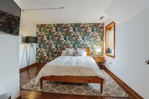 A bedroom with a floral wallpaper, a wooden bed, a nightstand, and a lamp. - Overlook Brandywine Valley (Thornton)