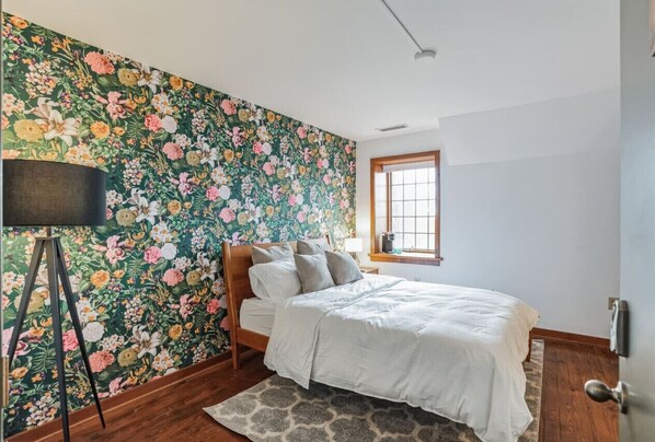 A bedroom with a floral wallpaper, a wooden bed, a bedside table, and a window. - Overlook Brandywine Valley (Thornton)