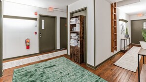 A hallway with wooden flooring, green rugs, a fire extinguisher, and a wooden cabinet with towels.