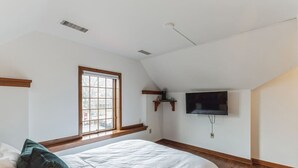 A bedroom with a bed, a window, a mounted TV, and wooden trim.