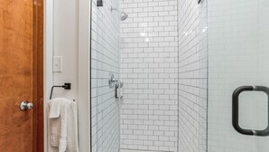 A shower with white tiles, a wooden door, and a towel rack.