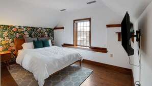 A bedroom with a bed, a window, a TV, and a floral wallpaper.