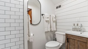 A bathroom with white tiled walls, a white toilet, a wooden cabinet, and a mirror. - Historic Thornton Studio Retreat (Thornton)