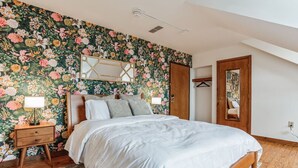 A bedroom with a floral wallpaper, a wooden bed, a nightstand with a lamp, and a mirror on the wall. - Historic Thornton Studio Retreat (Thornton)