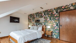 A bedroom with a wooden bed, a gray patterned rug, a wooden nightstand, a mirror, and a door. - Historic Thornton Studio Retreat (Thornton)
