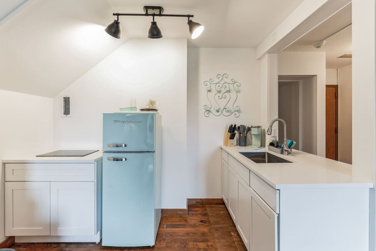 A compact kitchen with a light blue refrigerator, white cabinetry, a sink, and a decorative wall piece.