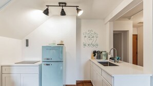 A compact kitchen with a light blue refrigerator, white cabinetry, a sink, and a decorative wall piece. - Thornton Studio w/ Kitchenette (Thornton)