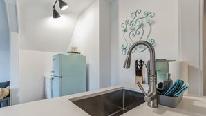 A modern kitchen with a stainless steel sink, a light blue refrigerator, and a decorative wall piece. - Thornton Studio w/ Kitchenette (Thornton)