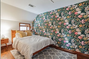 Relax in this serene bedroom with a large bed, floral wallpaper, and a cozy reading nook.