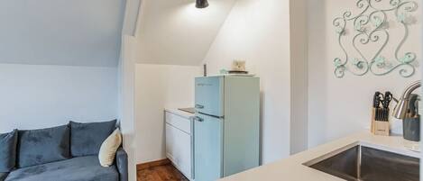 A compact living space with a sofa, a small kitchenette, and a decorative wall piece.
